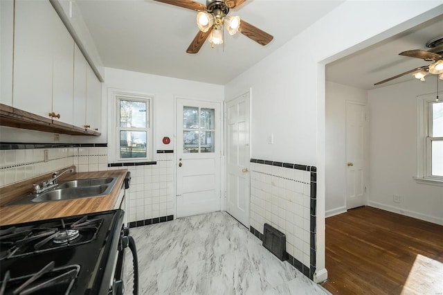kitchen with ceiling fan, a sink, white cabinets, butcher block countertops, and gas range oven