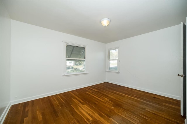 spare room featuring baseboards and dark wood finished floors