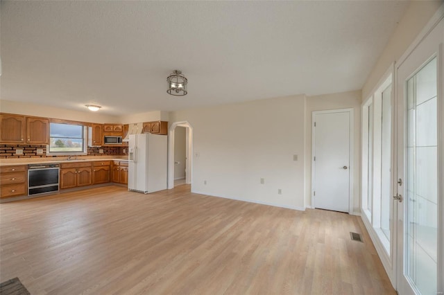 kitchen with appliances with stainless steel finishes, sink, light wood-type flooring, and decorative backsplash