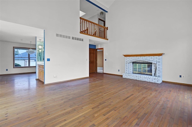 unfurnished living room with a high ceiling, a chandelier, hardwood / wood-style flooring, and a brick fireplace