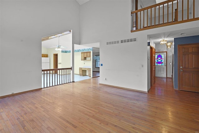 unfurnished living room with a high ceiling, hardwood / wood-style floors, and ceiling fan with notable chandelier