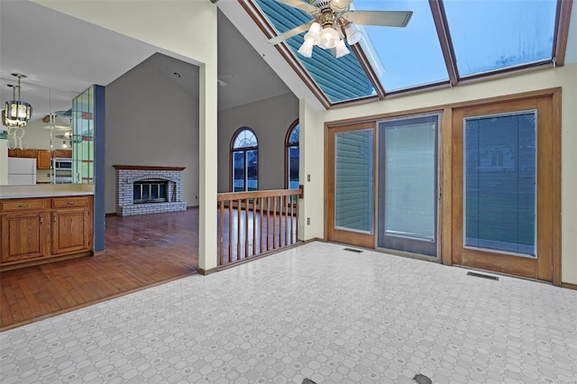 unfurnished living room with lofted ceiling, hardwood / wood-style floors, ceiling fan with notable chandelier, and a brick fireplace