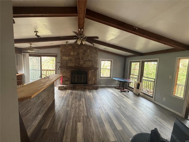 unfurnished living room featuring dark hardwood / wood-style flooring, ceiling fan, a stone fireplace, and vaulted ceiling with beams