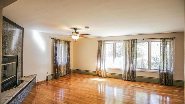 unfurnished living room featuring a tiled fireplace, hardwood / wood-style flooring, a baseboard radiator, and ceiling fan