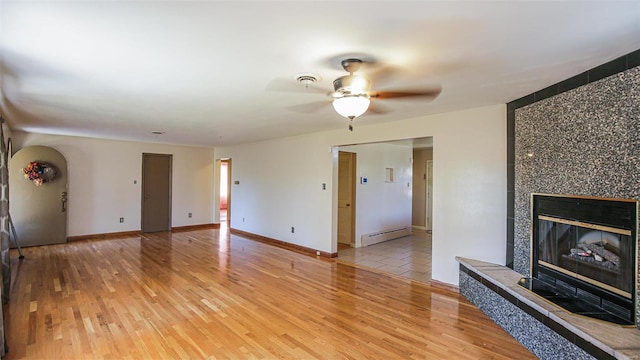 unfurnished living room with a baseboard radiator, a tiled fireplace, light hardwood / wood-style flooring, and ceiling fan