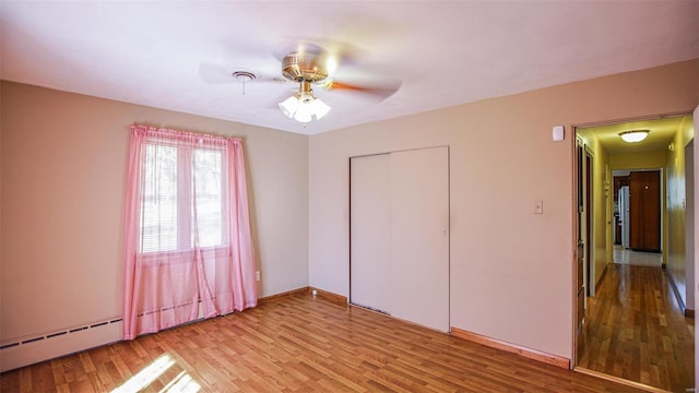 unfurnished bedroom with a closet, a baseboard heating unit, light hardwood / wood-style floors, and ceiling fan