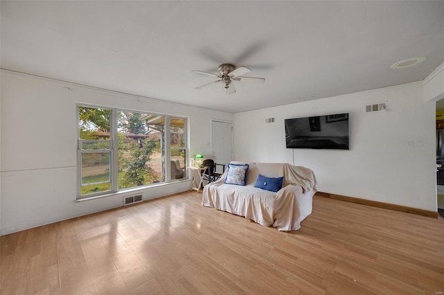 living area featuring ceiling fan, light wood-type flooring, and crown molding