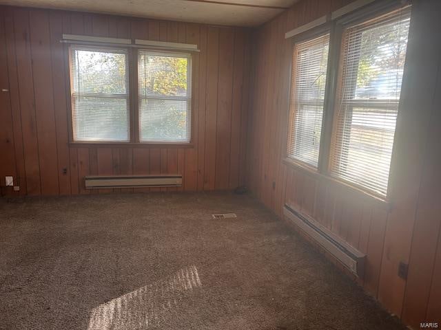 carpeted spare room featuring wooden walls and baseboard heating