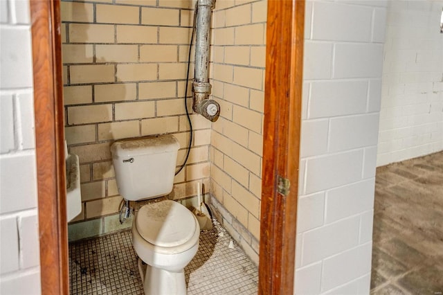 bathroom with toilet, tile patterned flooring, and brick wall