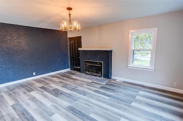 unfurnished living room featuring a brick fireplace, wood-type flooring, and a notable chandelier