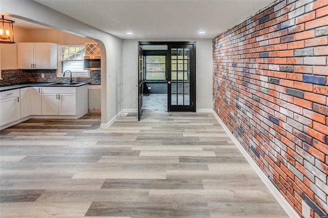 kitchen with white cabinetry, decorative backsplash, brick wall, and sink