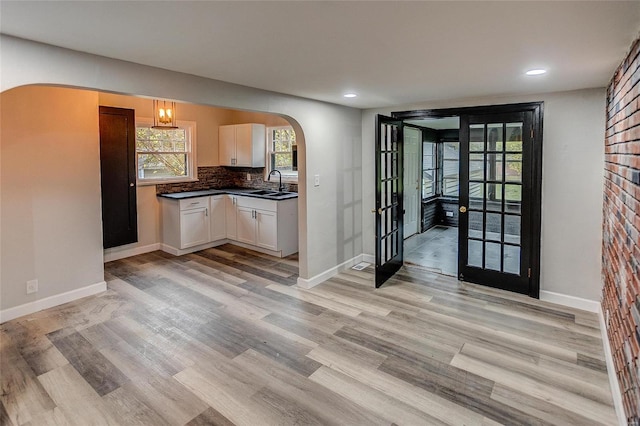 kitchen with tasteful backsplash, french doors, white cabinetry, sink, and light hardwood / wood-style flooring