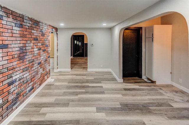 hallway featuring light hardwood / wood-style flooring and brick wall