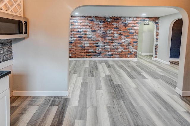 unfurnished dining area with brick wall and light wood-type flooring