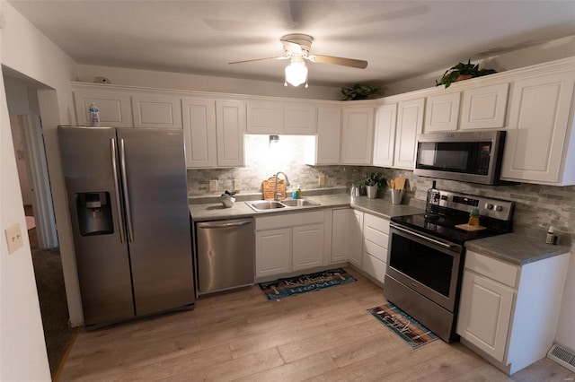 kitchen with white cabinets, sink, light hardwood / wood-style flooring, decorative backsplash, and appliances with stainless steel finishes