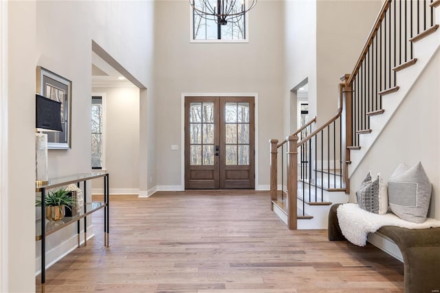 entrance foyer featuring light wood-type flooring, ornamental molding, a high ceiling, and french doors