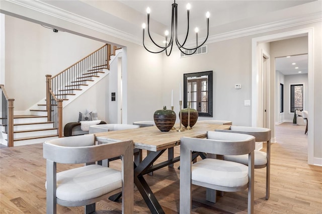 dining space with light wood-type flooring, crown molding, and an inviting chandelier