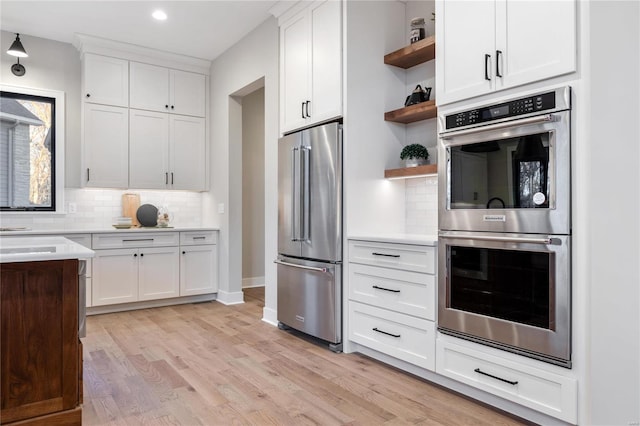 kitchen with white cabinets, light wood-type flooring, backsplash, and appliances with stainless steel finishes