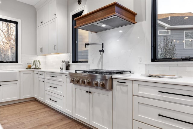 kitchen with decorative backsplash, custom range hood, stainless steel gas cooktop, white cabinets, and light hardwood / wood-style floors