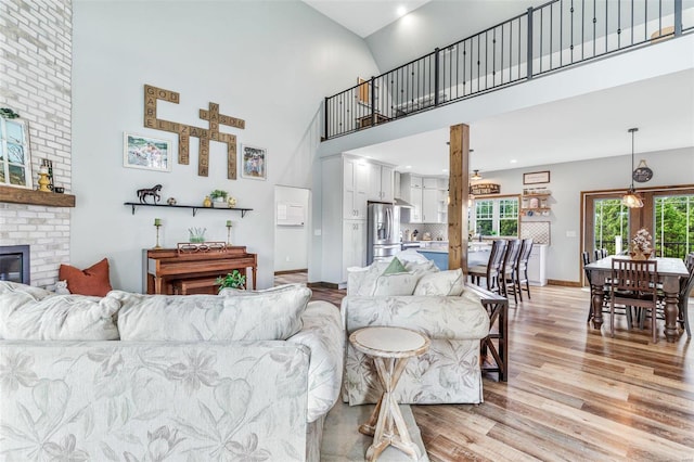 living room featuring high vaulted ceiling, a brick fireplace, and light hardwood / wood-style flooring