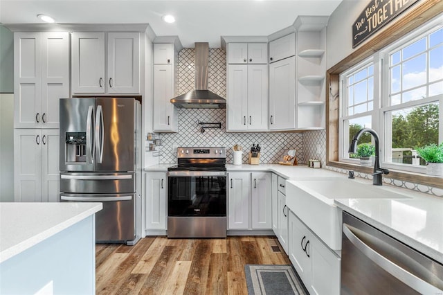 kitchen featuring a wealth of natural light, wood-type flooring, wall chimney exhaust hood, and stainless steel appliances