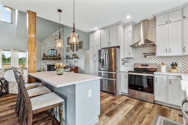 kitchen with pendant lighting, wall chimney range hood, appliances with stainless steel finishes, and white cabinets