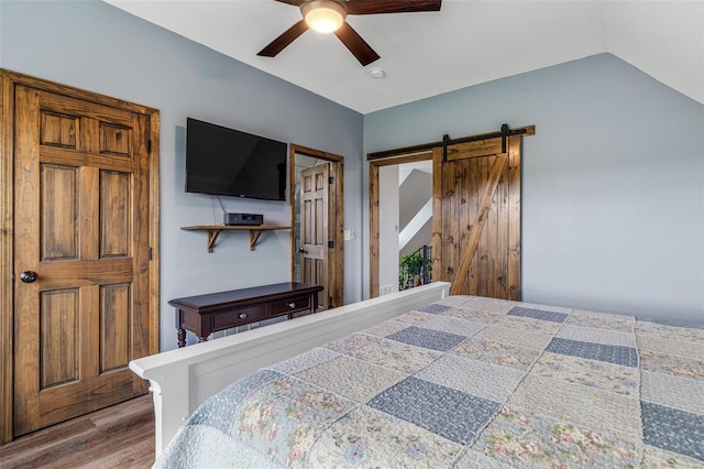 bedroom with a barn door, ceiling fan, lofted ceiling, and wood-type flooring