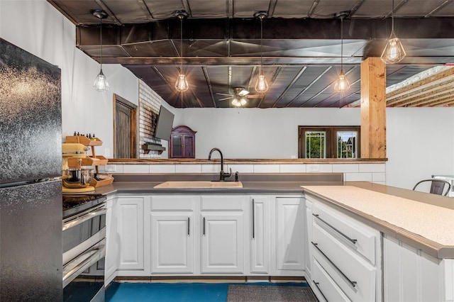 kitchen with white cabinetry, black fridge, sink, pendant lighting, and stainless steel range