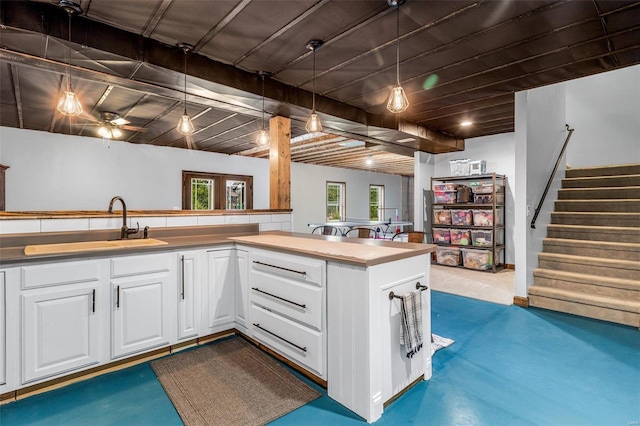 kitchen featuring white cabinets, kitchen peninsula, hanging light fixtures, and concrete flooring