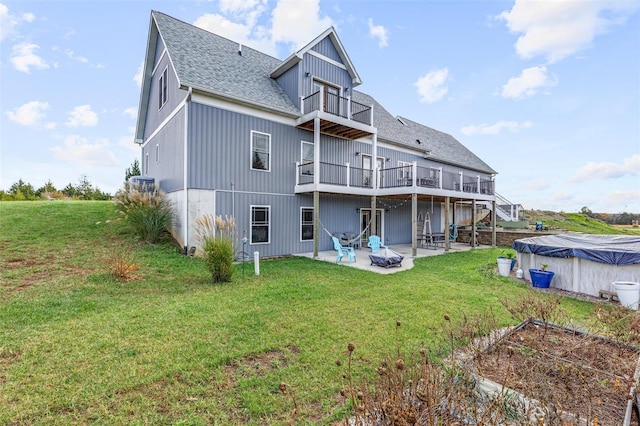 rear view of house with a balcony, a yard, and a patio