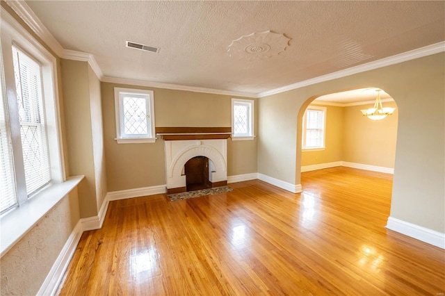 unfurnished living room featuring wood-type flooring, a textured ceiling, a brick fireplace, and crown molding