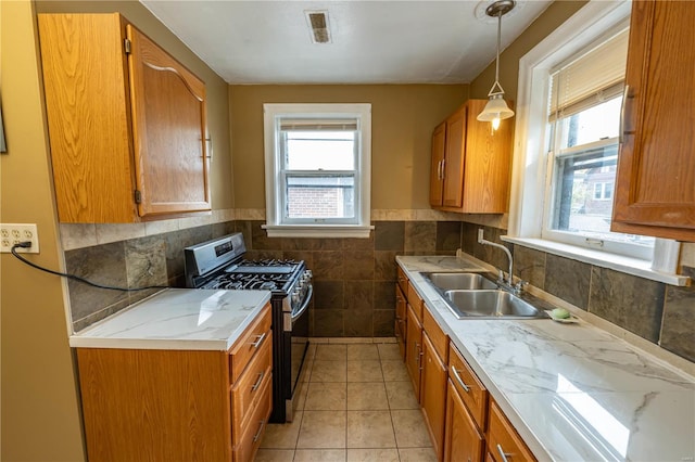 kitchen featuring gas stove, light stone countertops, sink, hanging light fixtures, and light tile patterned flooring