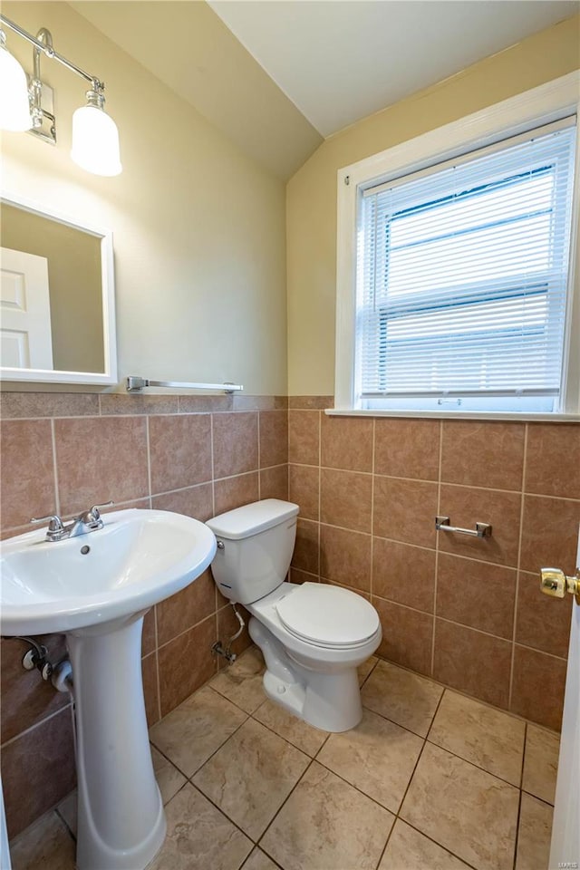 bathroom featuring lofted ceiling, sink, tile patterned flooring, toilet, and tile walls