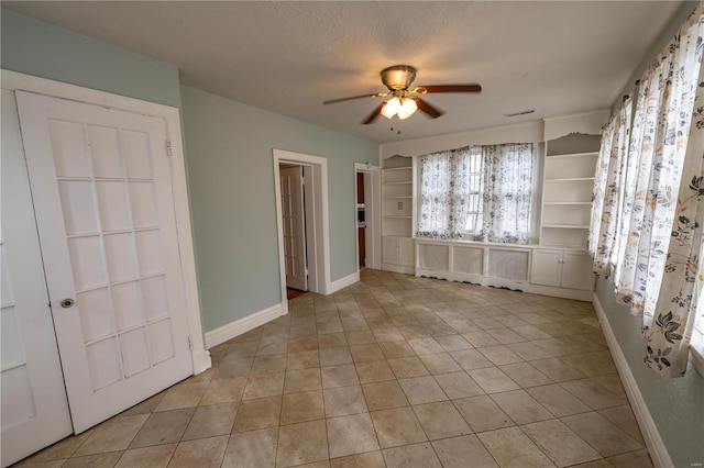 tiled spare room featuring ceiling fan, a textured ceiling, and built in shelves