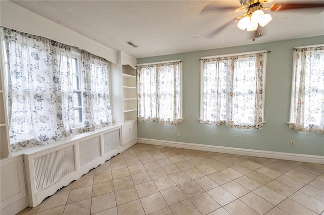 tiled spare room featuring plenty of natural light, ceiling fan, and radiator heating unit