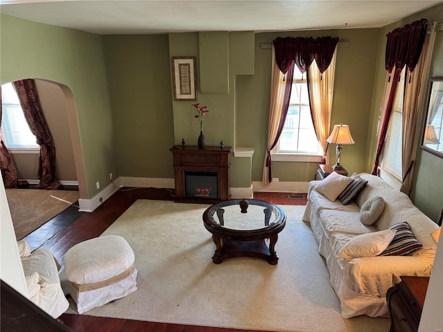 living area featuring a lit fireplace, arched walkways, dark wood finished floors, and baseboards