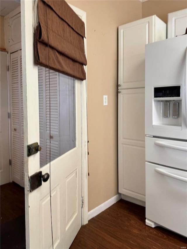 kitchen with white fridge with ice dispenser, dark wood-style flooring, white cabinetry, and baseboards