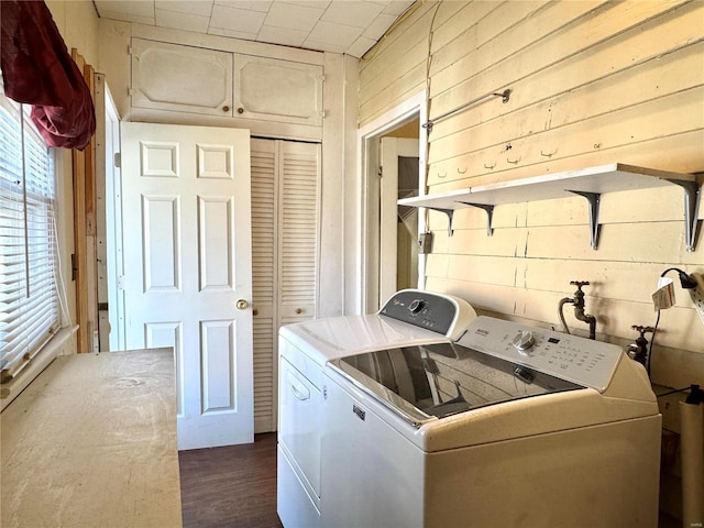 washroom featuring laundry area, wooden walls, washer and clothes dryer, and dark wood-type flooring