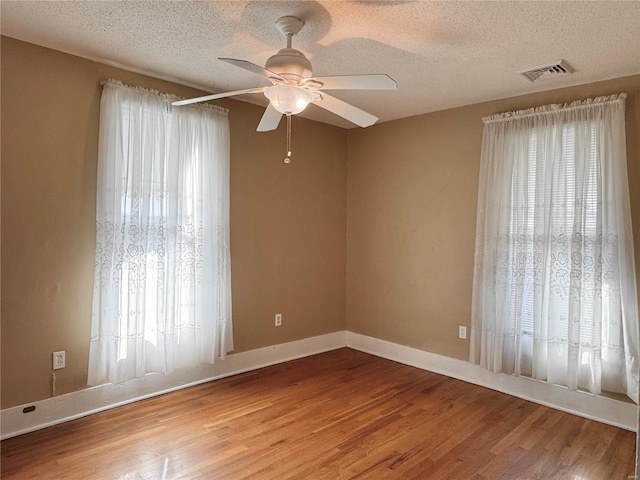 unfurnished room featuring visible vents, light wood-style floors, a ceiling fan, a textured ceiling, and baseboards