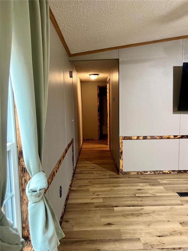 corridor with lofted ceiling, a textured ceiling, ornamental molding, and light wood-type flooring