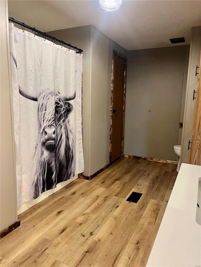 bathroom with toilet, hardwood / wood-style floors, curtained shower, and a textured ceiling