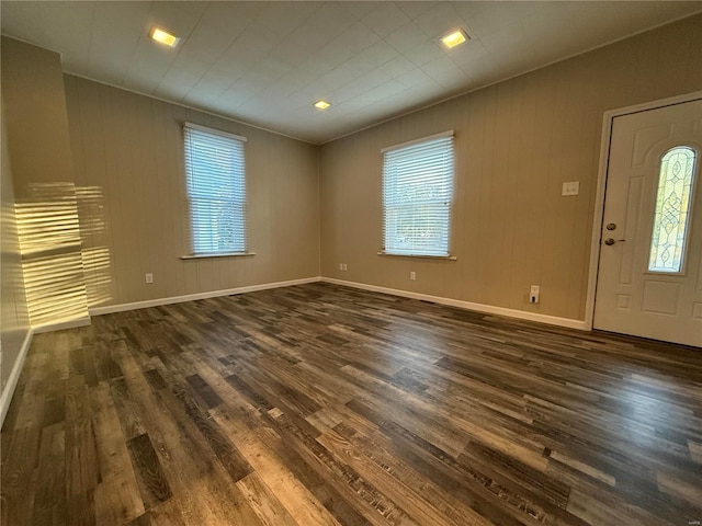 entrance foyer featuring a wealth of natural light, wooden walls, and dark hardwood / wood-style floors