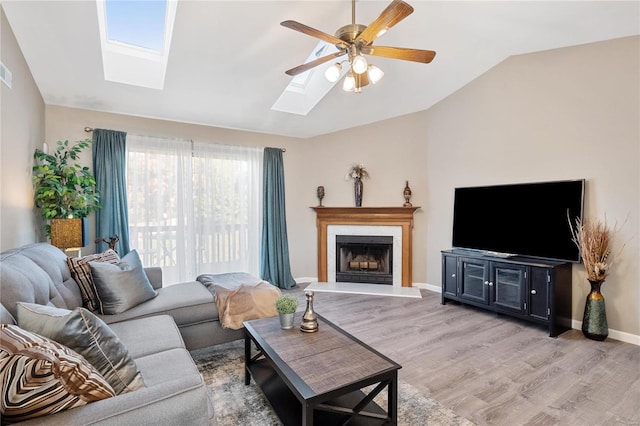 living room featuring light hardwood / wood-style floors, ceiling fan, and vaulted ceiling with skylight