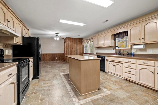 kitchen with a center island, black appliances, wooden walls, sink, and ceiling fan