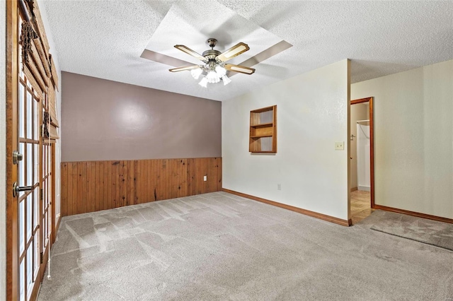 carpeted empty room featuring wood walls, a textured ceiling, and ceiling fan