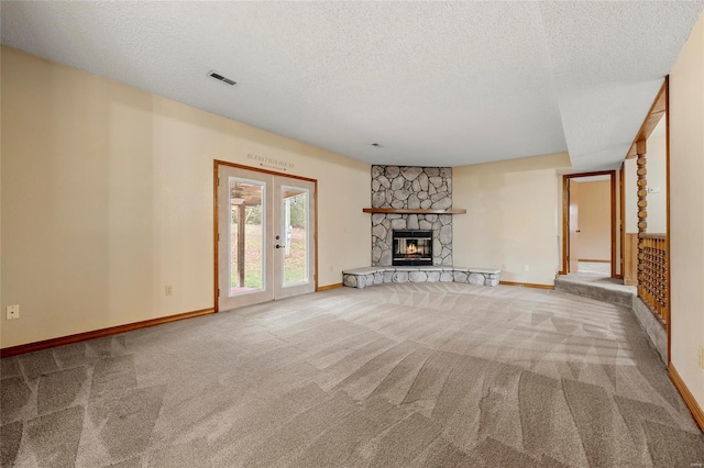 unfurnished living room featuring a stone fireplace, french doors, carpet floors, and a textured ceiling