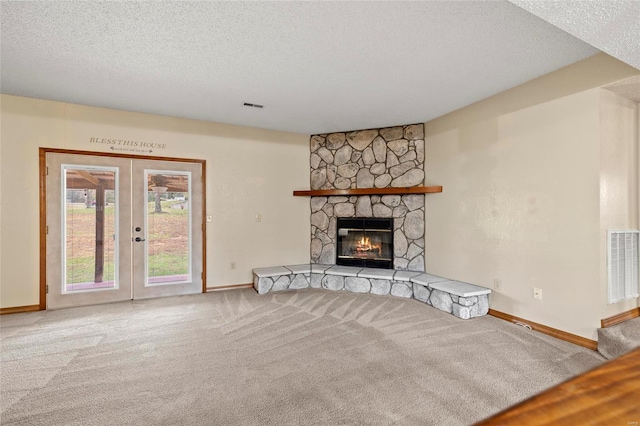 unfurnished living room with a fireplace, light colored carpet, a textured ceiling, and french doors