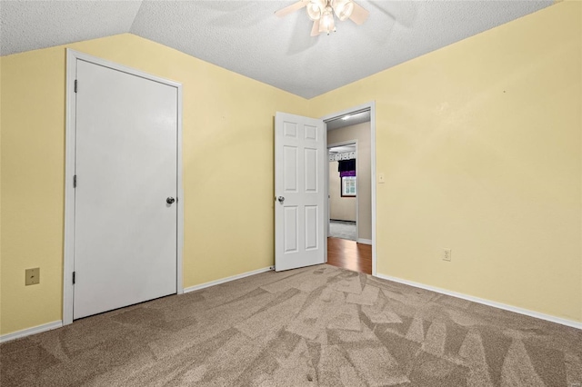 unfurnished bedroom with a textured ceiling, carpet floors, ceiling fan, and vaulted ceiling