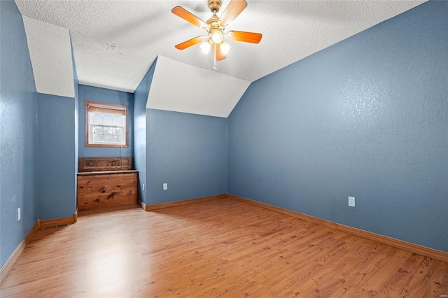 additional living space featuring light wood-type flooring, vaulted ceiling, ceiling fan, and a textured ceiling