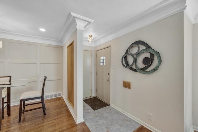 foyer entrance featuring light wood finished floors, baseboards, visible vents, and ornamental molding